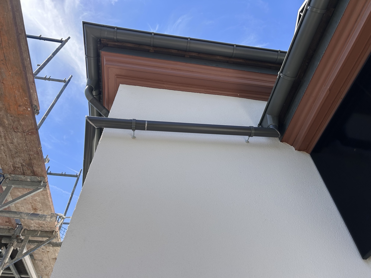 Dunkle Dachrinnen mit angepassten Rohrbögen und einer Verbindungsleitung entlang der hell verputzten Fassade