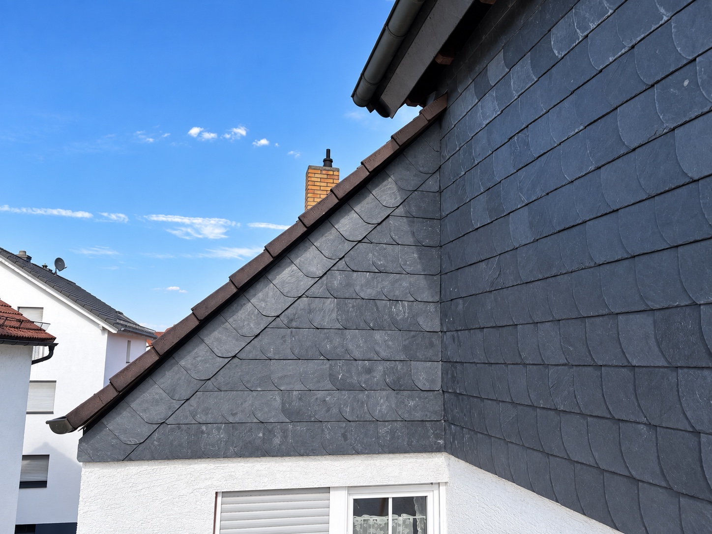 Dunkle Schieferbekleidung an Giebel und Fassade mit angepasstem Verlauf entlang der Dachschräge und dem Gebäudeeck